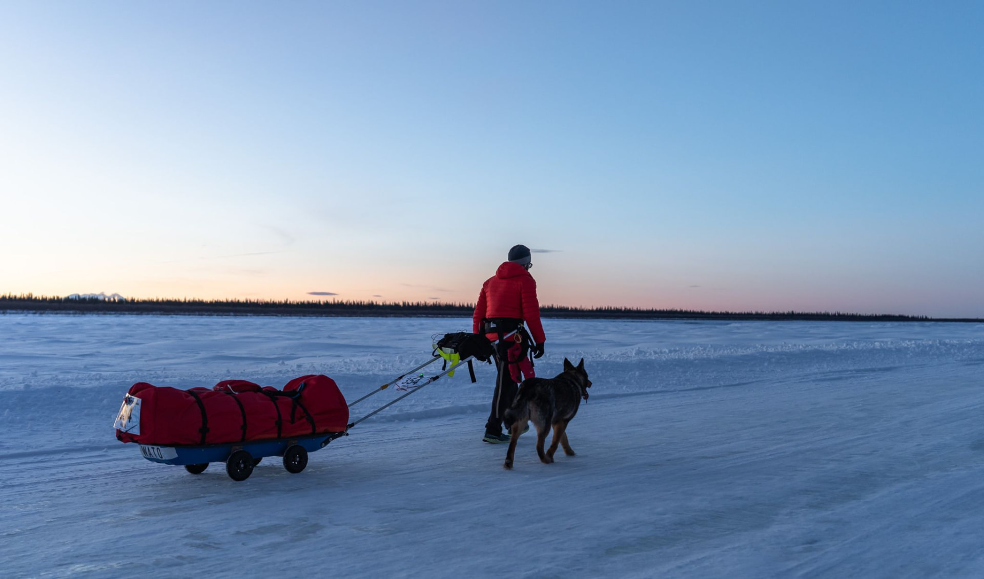 Paul Watkins pulling a sled across a frozen river at dusk
