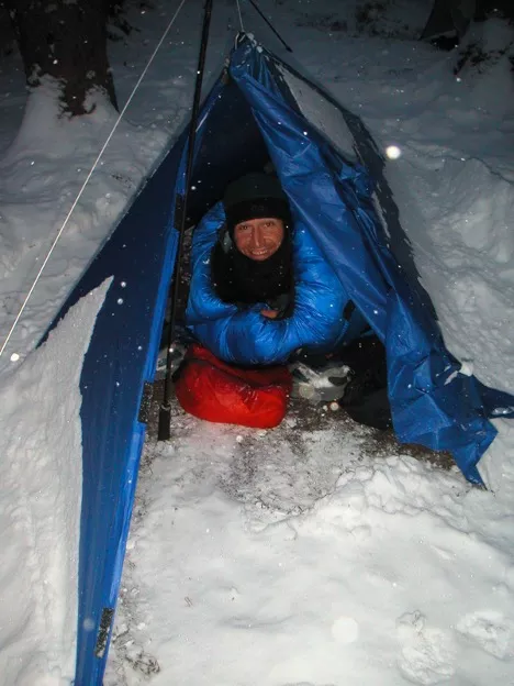 Glen Van Peski in a tarp shelter during a winter snowstorm